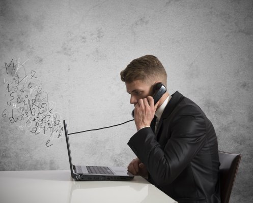 man in suit speaking on the phone in front of laptop small business phone systems